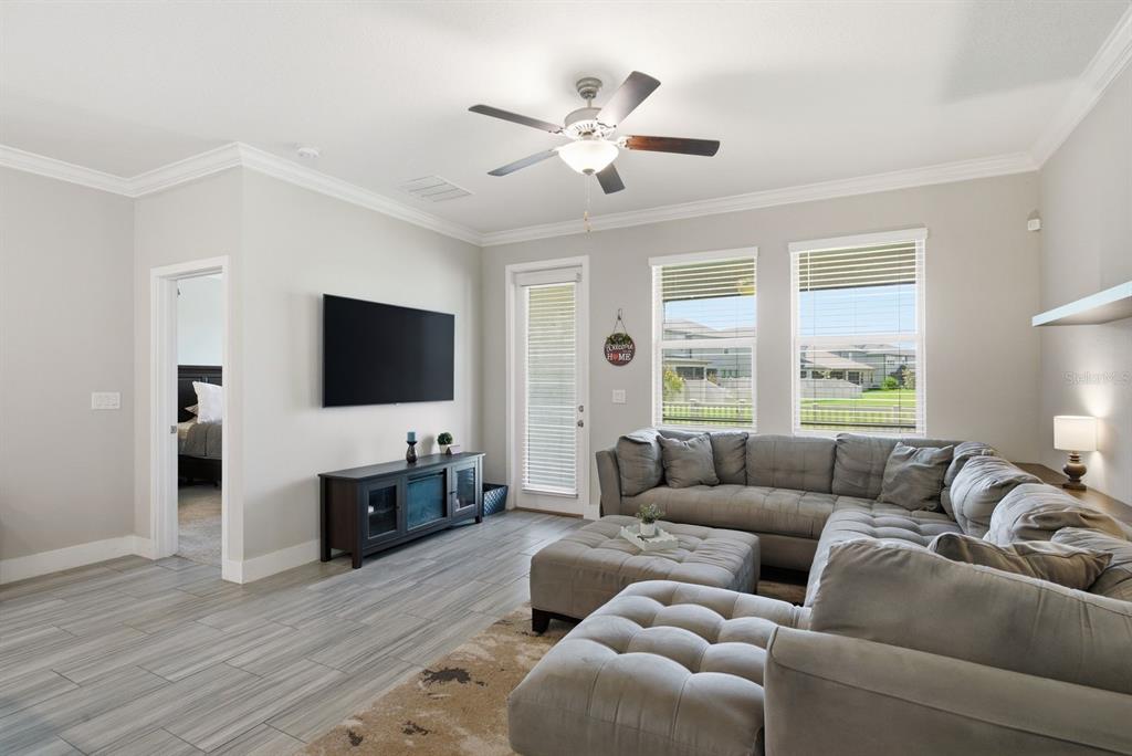 A living room features a gray sectional sofa, a wall-mounted television, and tile flooring — 8683 WINNING FIELDS ROAD, NEW PORT RICHEY, FL