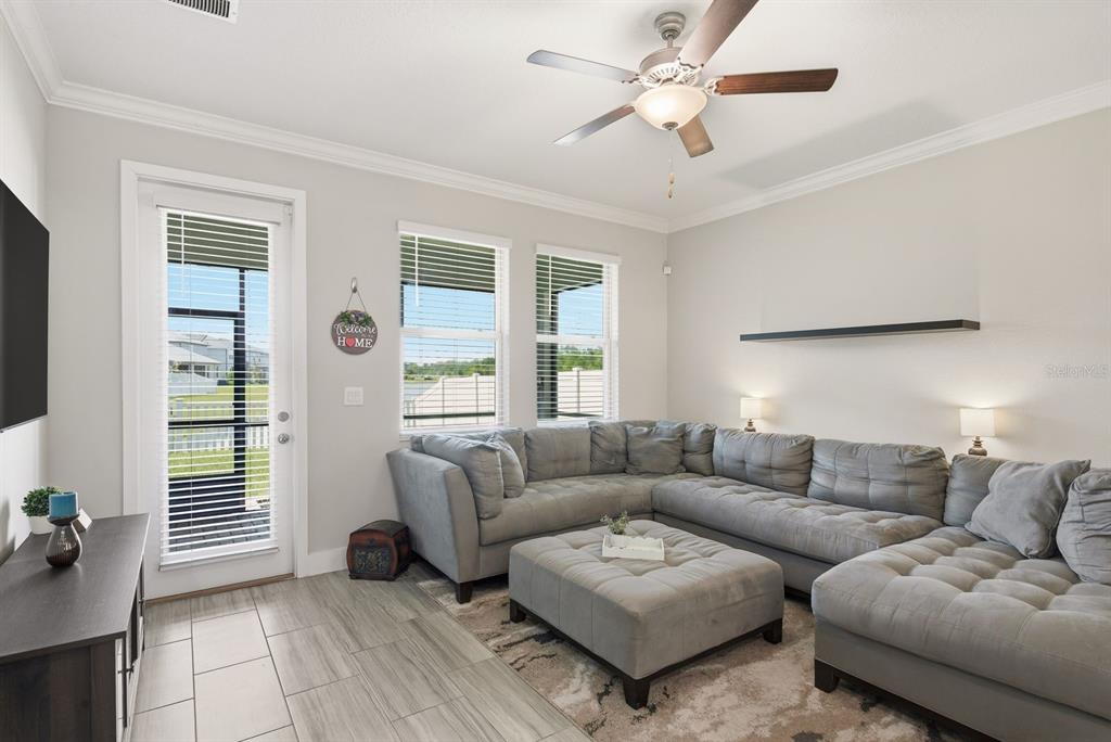 A living room features a gray sectional sofa, a matching ottoman, and a glass door — 8683 WINNING FIELDS ROAD, NEW PORT RICHEY, FL