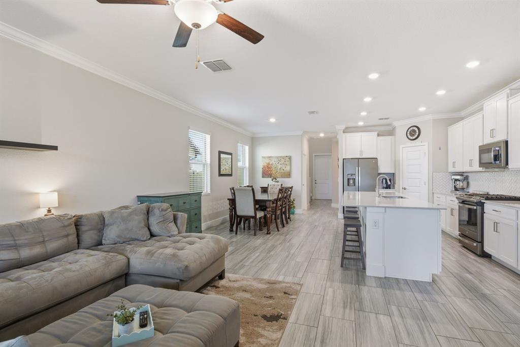 An open-concept living room and kitchen featuring gray tile floors and white cabinetry — 8683 WINNING FIELDS ROAD, NEW PORT RICHEY, FL