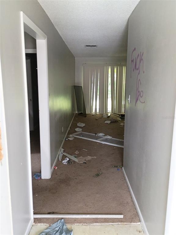 A damaged interior hallway leads to a living area with sliding glass doors and debris — 7272 BALBOA DRIVE UNIT 7272, ORLANDO, FL