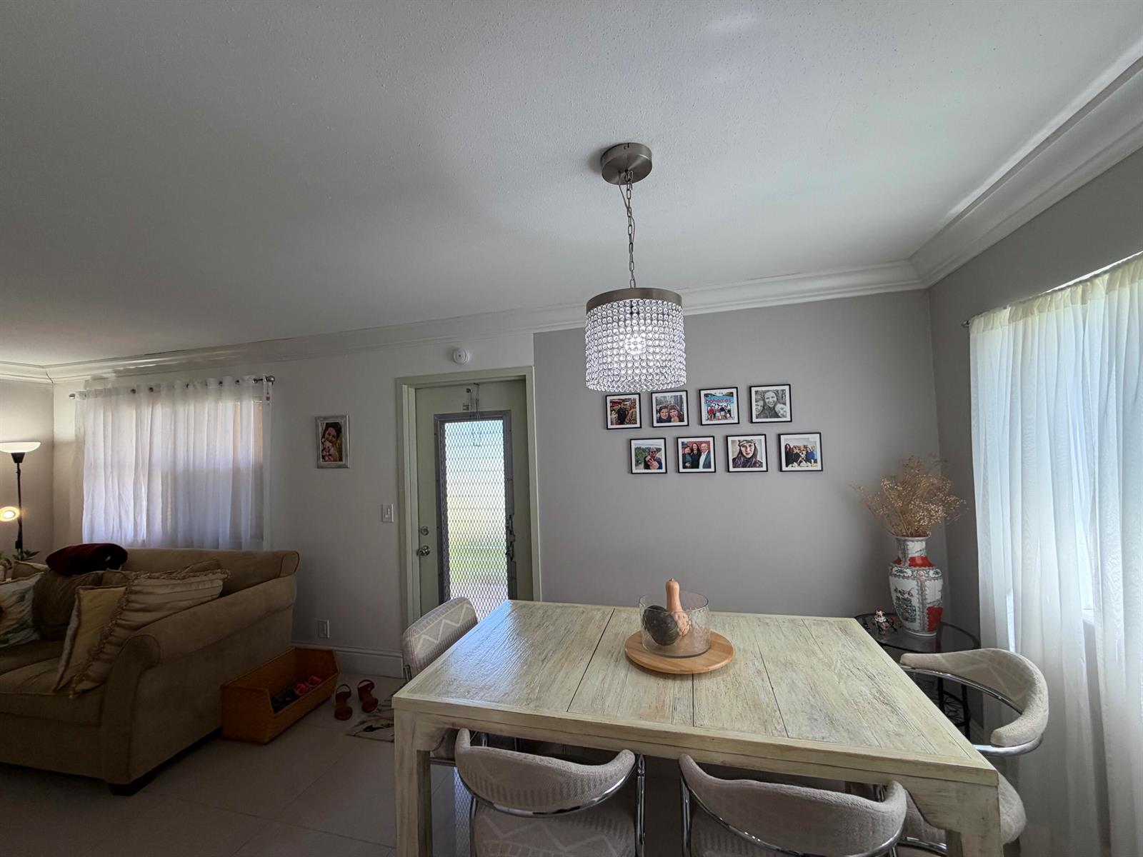 A dining area features a light wood table, a crystal chandelier, and a gallery wall — 292 Brittany G # 292, Delray Beach FL 33446, DELRAY BEACH, FL