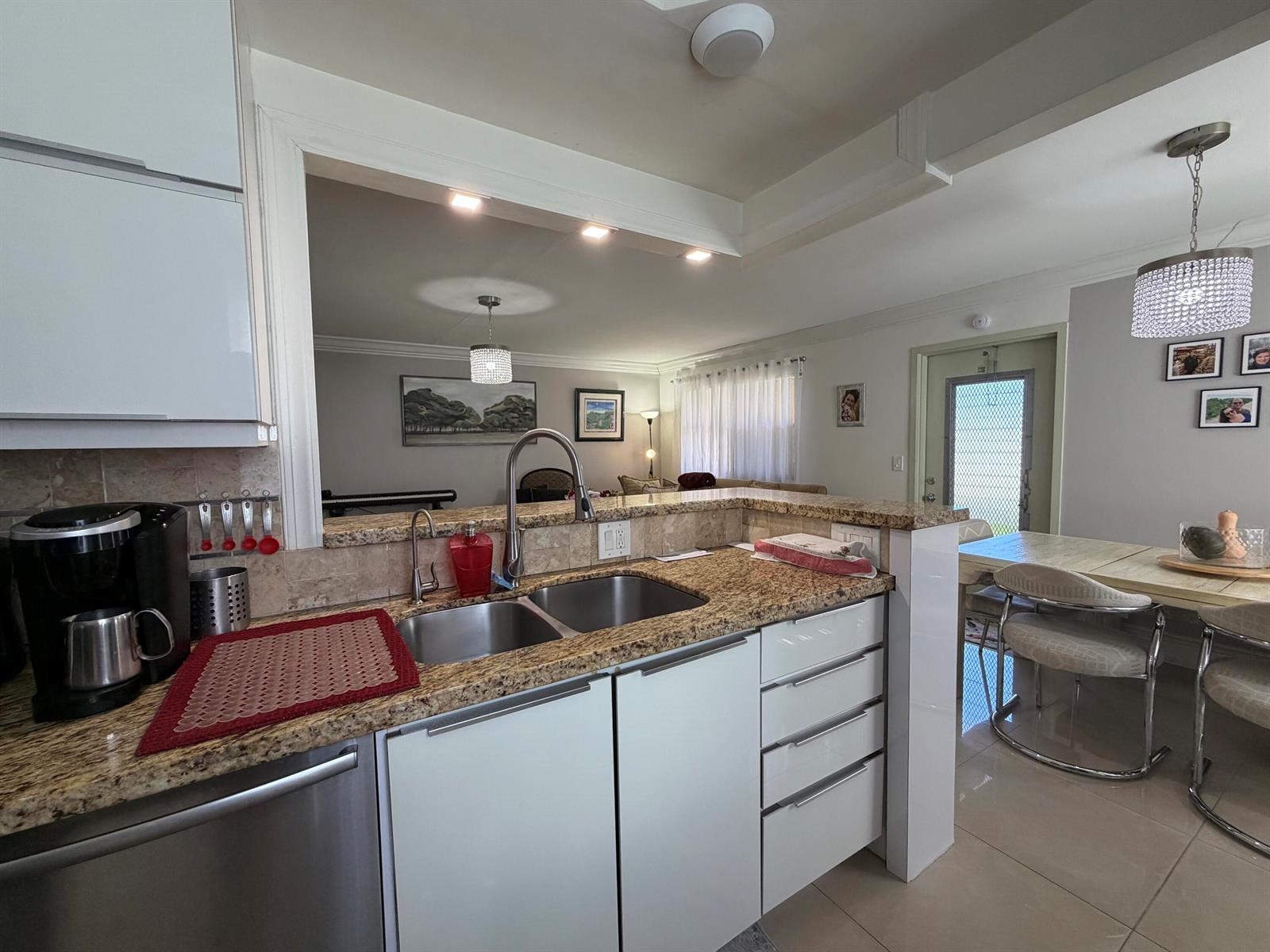 A kitchen with granite countertops and white cabinets overlooks a living area and dining space — 292 Brittany G # 292, Delray Beach FL 33446, DELRAY BEACH, FL