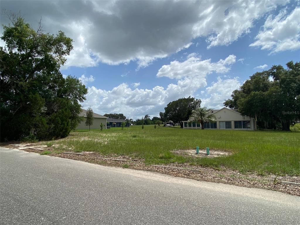 A vacant, grassy residential lot sits between two existing houses under a cloudy sky — Lot 194 CHESTNUT RIDGE ROAD, DADE CITY, FL