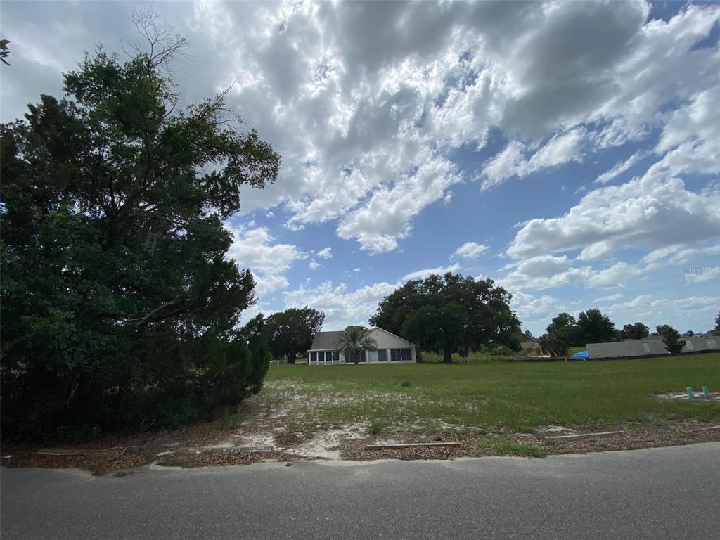 A grassy vacant lot sits in front of a single-story house under a cloudy sky — Lot 194 CHESTNUT RIDGE ROAD, DADE CITY, FL