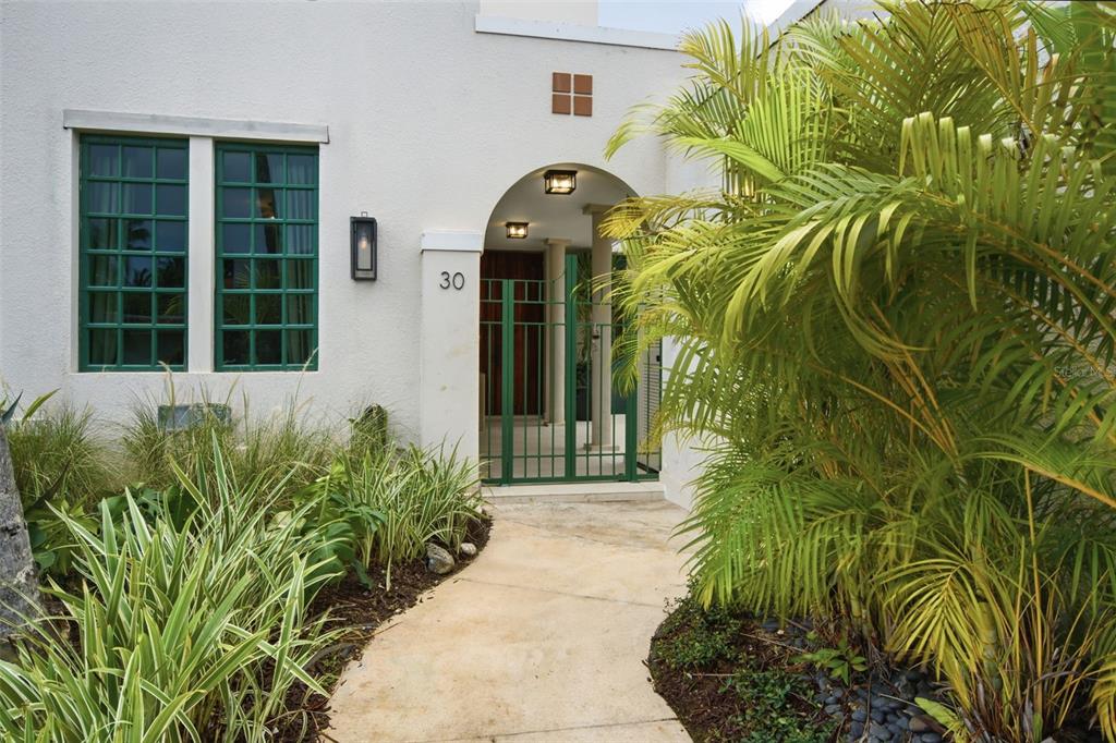 A concrete walkway leads to the gated arched entryway of a white stucco house — 30 CALLE ARENAS, DORADO, PR