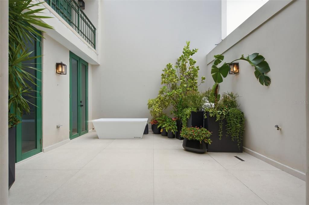 A white soaking tub sits on a tiled patio surrounded by potted plants and walls — 30 CALLE ARENAS, DORADO, PR
