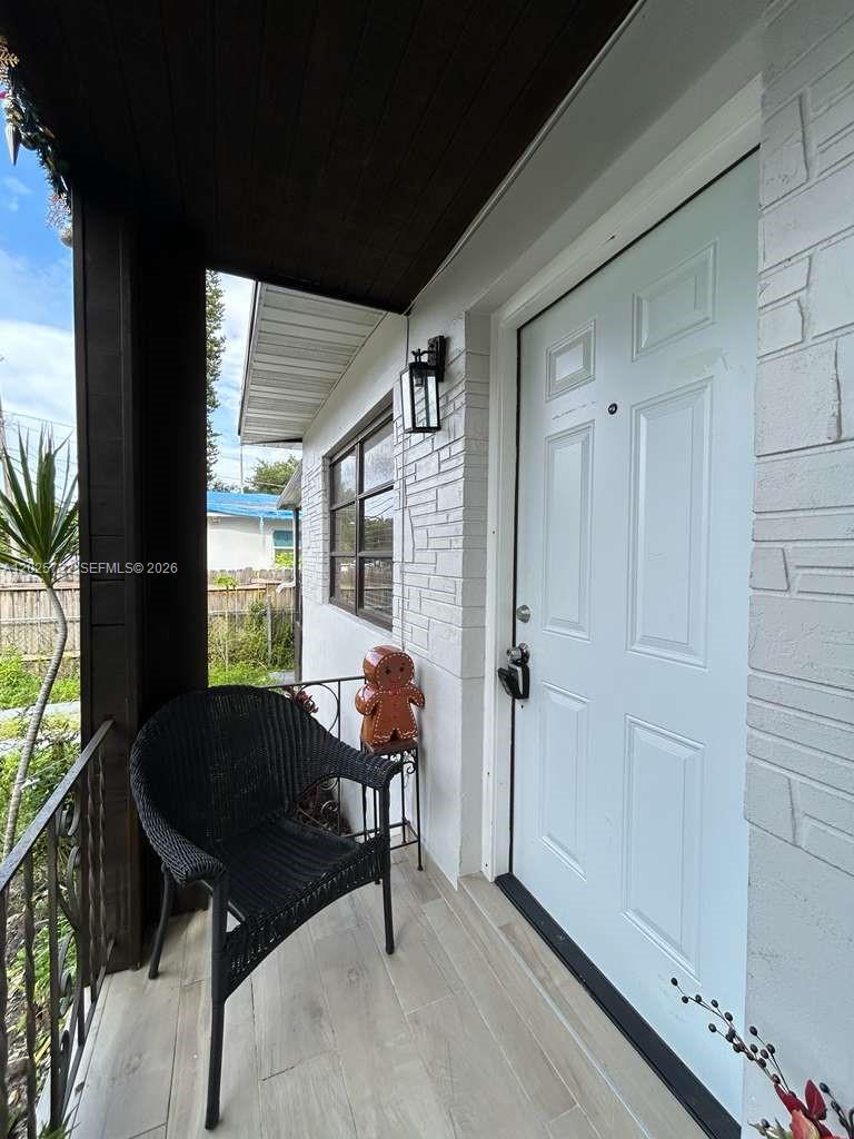 A covered front porch features a black wicker chair, a gingerbread man decoration, and white brick — 110 NW 58th St # 0, Miami FL 33127, MIAMI, FL