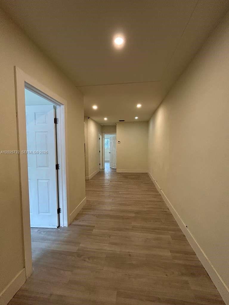 A hallway with light-colored wood-look flooring leads to a doorway in the distance — 110 NW 58th St # 0, Miami FL 33127, MIAMI, FL