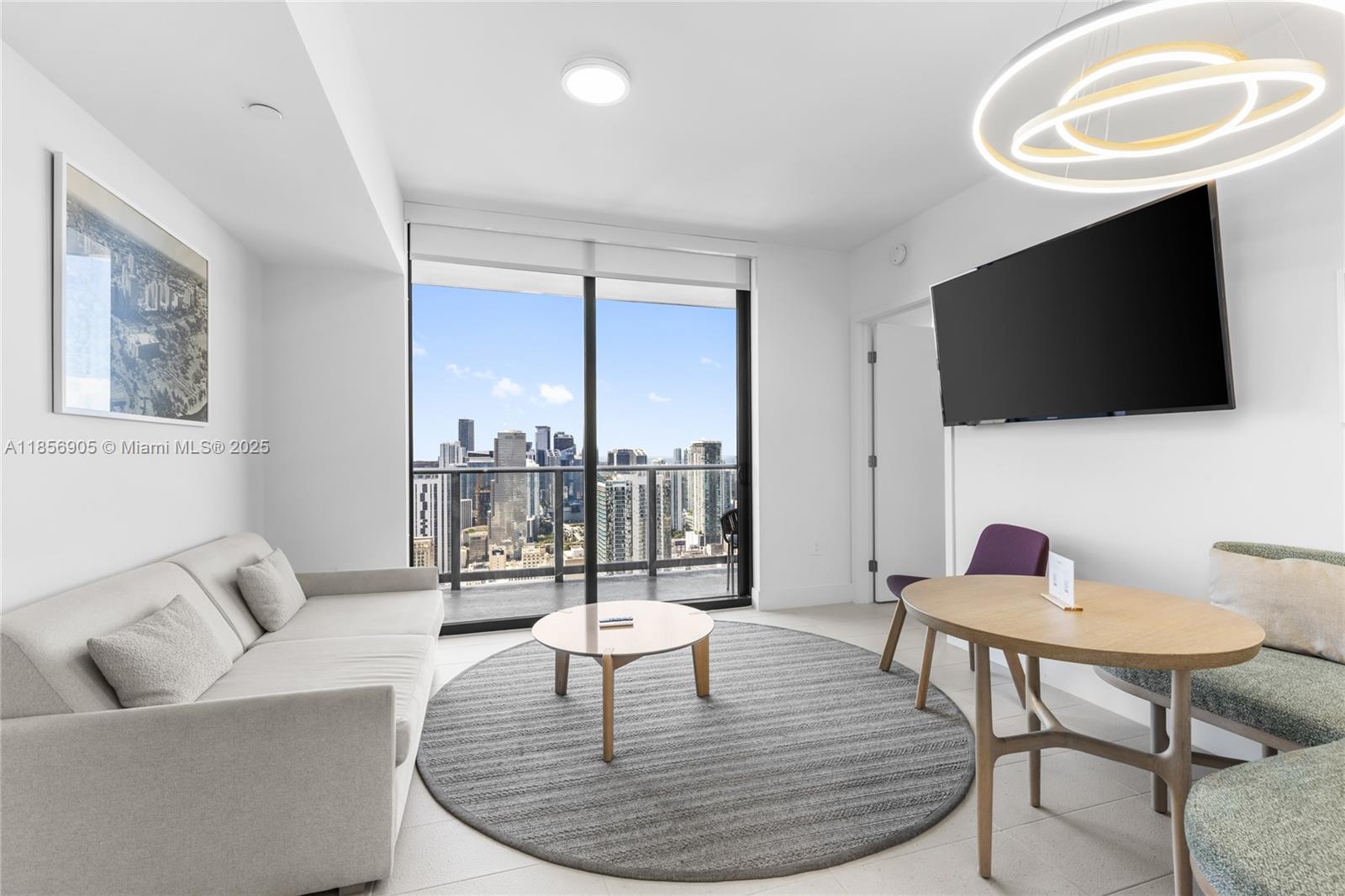 A modern living room features a sofa, circular rug, dining table, and floor-to-ceiling city views — 601 NE 1st Ave # 4607, Miami FL 33132, MIAMI, FL