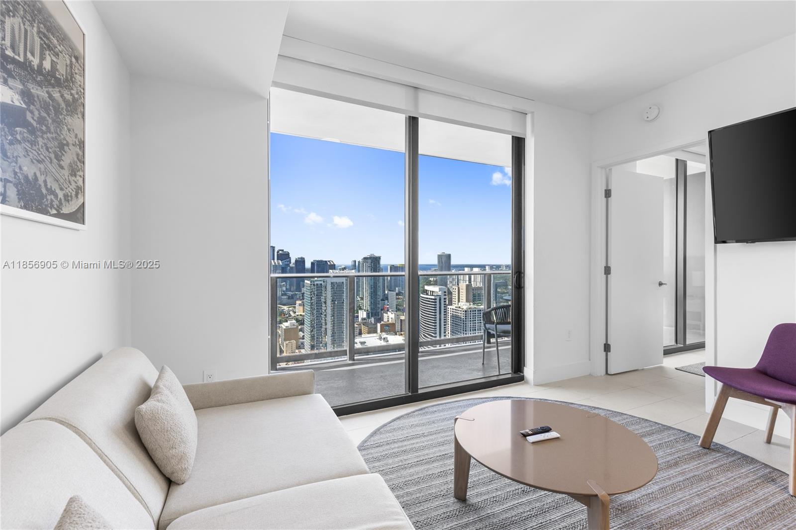 A modern living room features a beige sofa, oval coffee table, and floor-to-ceiling balcony windows — 601 NE 1st Ave # 4607, Miami FL 33132, MIAMI, FL