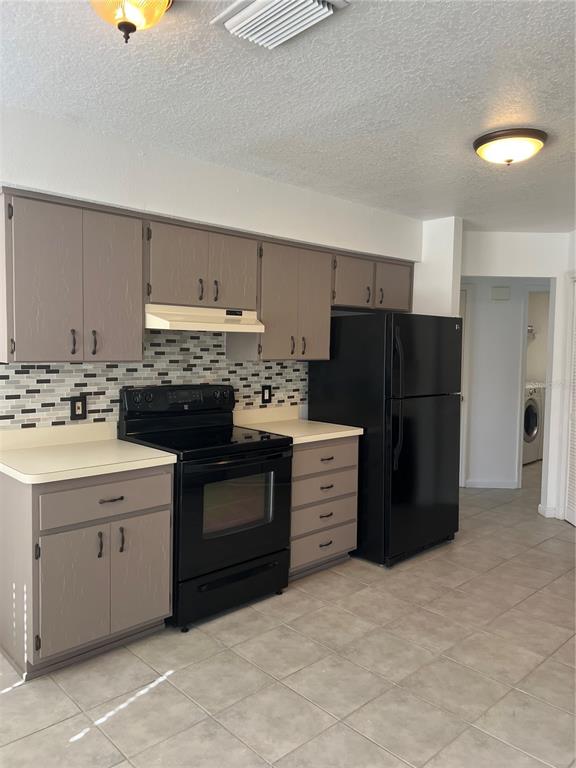 A kitchen features gray cabinets, a black stove, a black refrigerator, and a tiled backsplash — 5307 EL CERRO DRIVE, NEW PORT RICHEY, FL