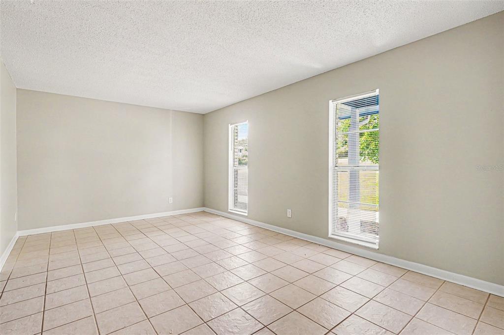 An empty room with beige walls, light-colored tile flooring, and two windows with blinds — 1534 HALLAM COURT S, LAKELAND, FL