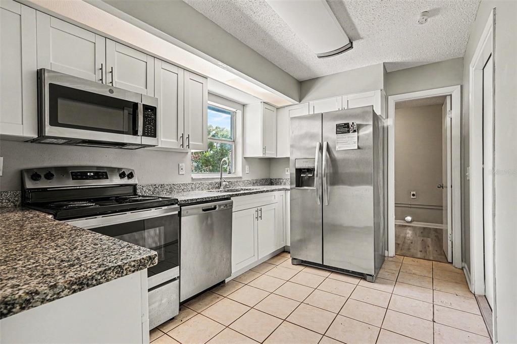 A kitchen with white cabinets, stainless steel appliances, granite countertops, and light-colored tile flooring — 1534 HALLAM COURT S, LAKELAND, FL