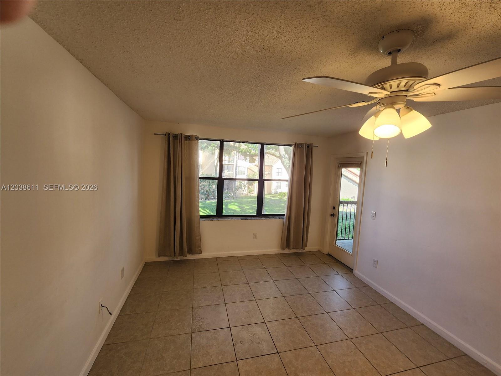 An empty room features beige tile flooring, a ceiling fan, and a sliding glass door — 4401 W Mcnab Rd # 16, Pompano Beach FL 33069, POMPANO BEACH, FL
