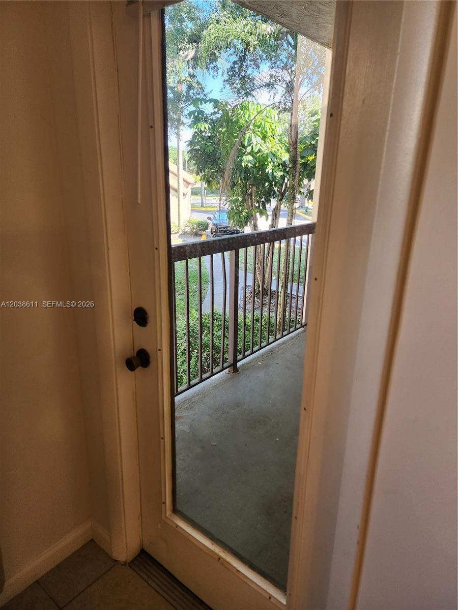 A glass door opens onto a small balcony with a metal railing overlooking trees — 4401 W Mcnab Rd # 16, Pompano Beach FL 33069, POMPANO BEACH, FL