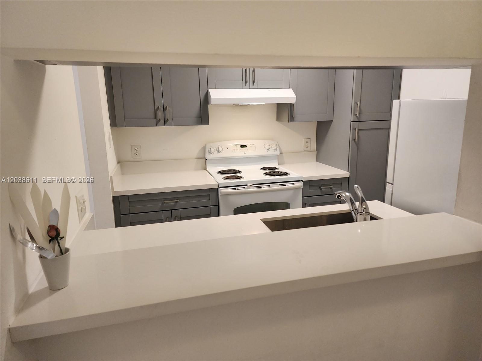 A kitchen features gray cabinets, white countertops, and a white stove viewed through a pass-through — 4401 W Mcnab Rd # 16, Pompano Beach FL 33069, POMPANO BEACH, FL