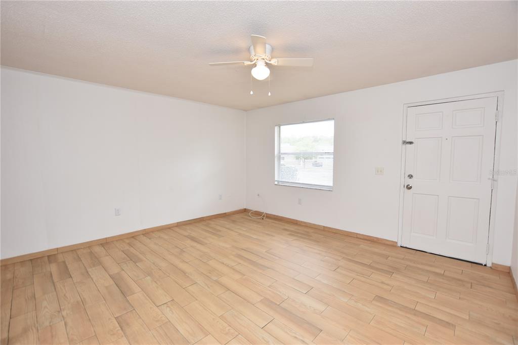 An empty room features white walls, light wood-look tile flooring, and a ceiling fan — 613 ROBIN ROAD UNIT 5, LAKELAND, FL
