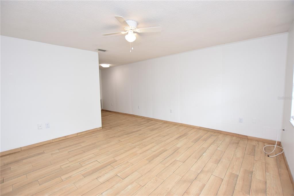 An empty room features white walls, a ceiling fan, and light wood-look tile flooring — 613 ROBIN ROAD UNIT 5, LAKELAND, FL