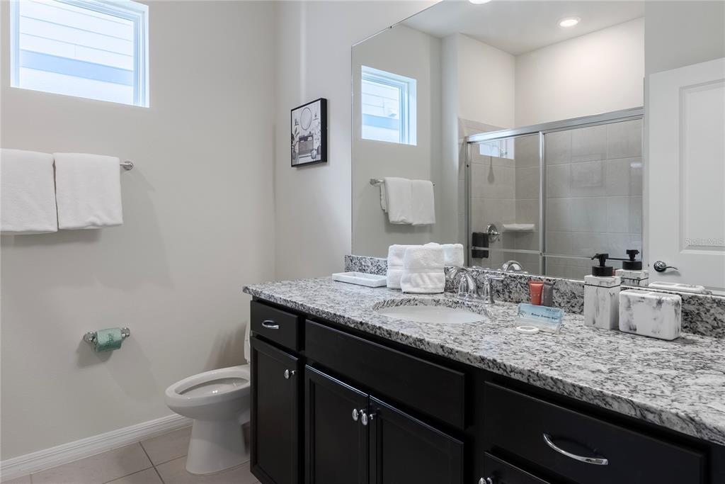 A bathroom features dark cabinets, a granite countertop, a toilet, and a glass-enclosed shower — 4425 KAIPO ROAD, DAVENPORT, FL