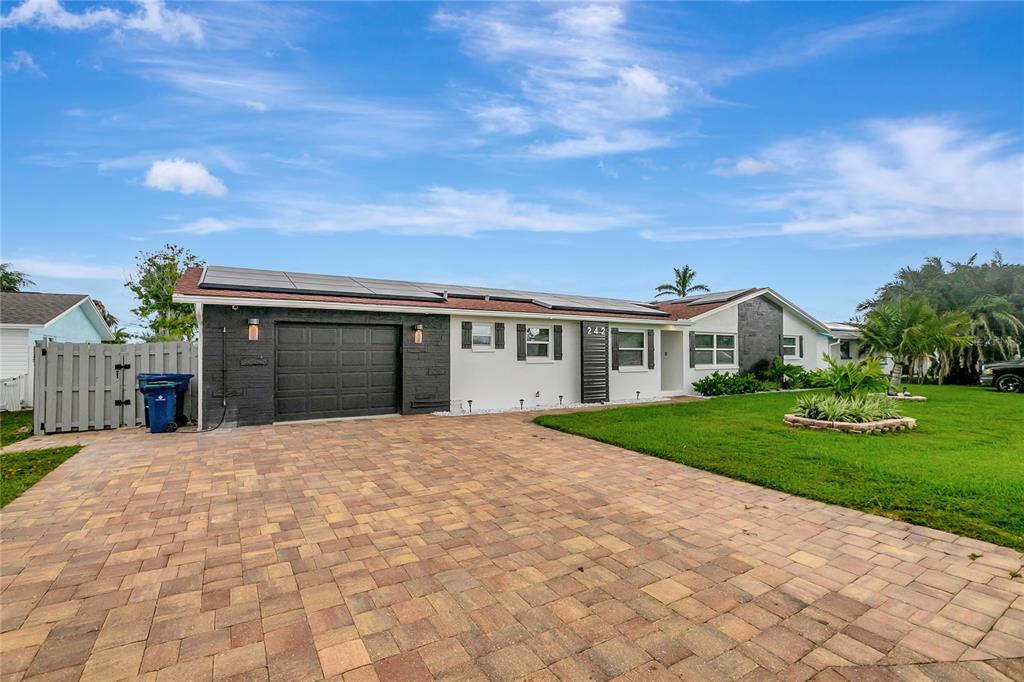 A single-story house with a paved driveway, solar panels, and a dark-painted garage — 242 176TH AVENUE E, REDINGTON SHORES, FL