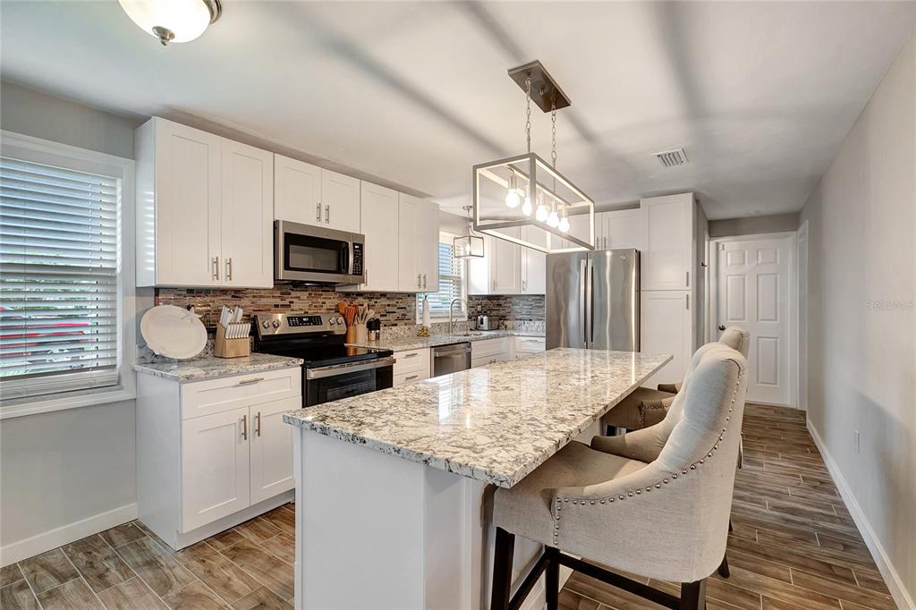 A kitchen features white cabinets, granite countertops, a center island, and stainless steel appliances — 242 176TH AVENUE E, REDINGTON SHORES, FL