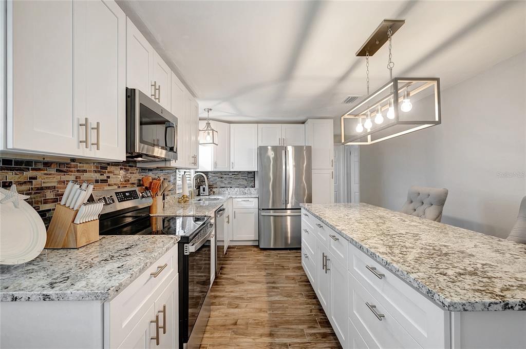 A kitchen with white cabinets, granite countertops, stainless steel appliances, and a large island — 242 176TH AVENUE E, REDINGTON SHORES, FL