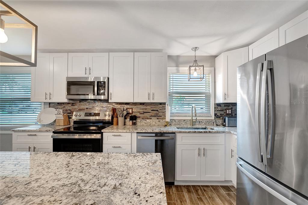 A kitchen features white cabinets, granite countertops, stainless steel appliances, and a tiled backsplash — 242 176TH AVENUE E, REDINGTON SHORES, FL