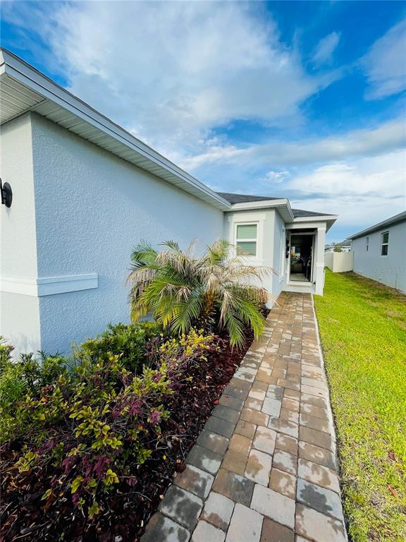 A paved walkway leads to the side entrance of a light-colored stucco house — 2818 SANCTUARY DRIVE, CLERMONT, FL
