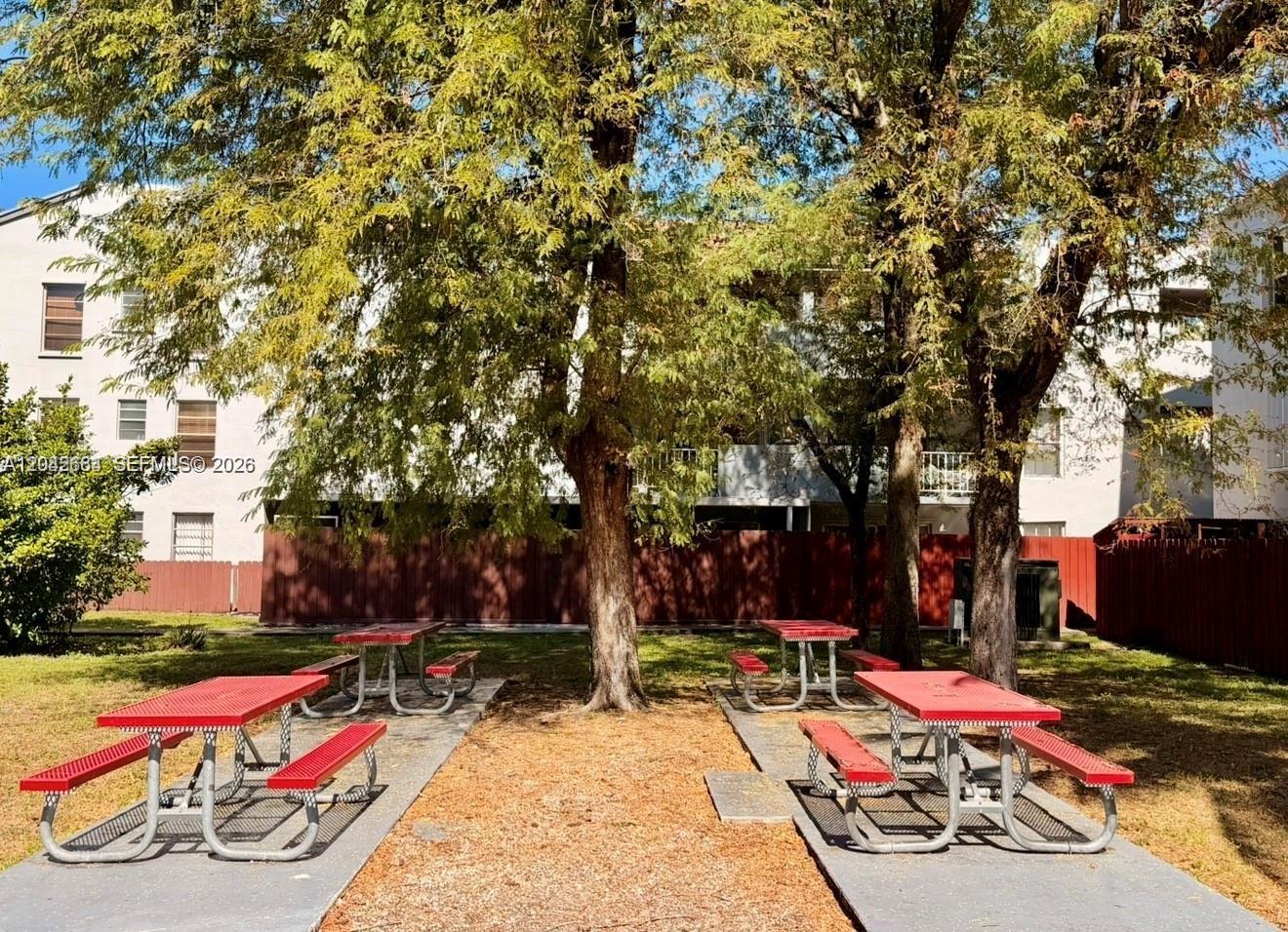 Four red picnic tables sit on concrete pads beneath trees in a residential courtyard — 1725 W 60th St # F202, Hialeah FL 33012, HIALEAH, FL