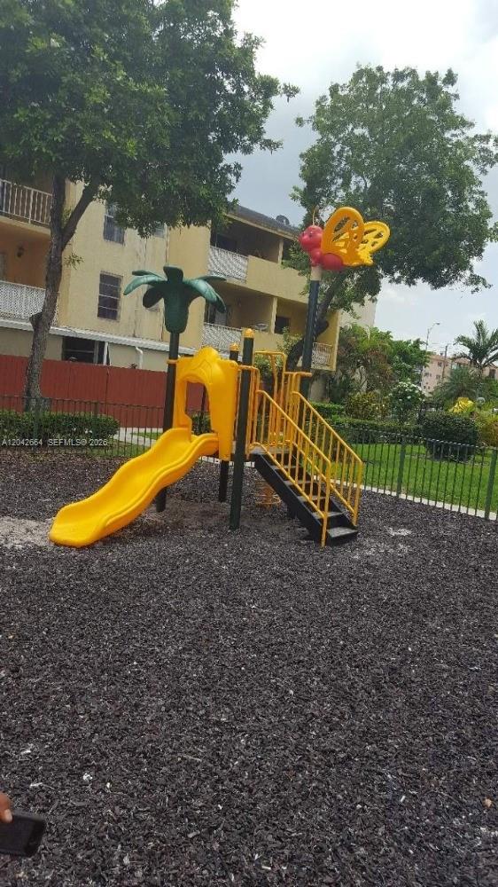 A yellow playground slide and stairs are located in a park with wood chip mulch — 1725 W 60th St # F202, Hialeah FL 33012, HIALEAH, FL