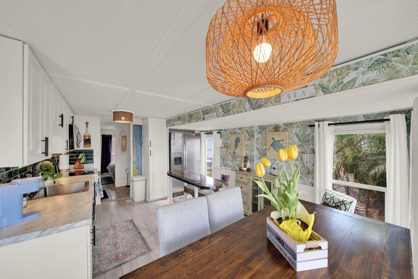 A kitchen and dining area with white cabinets, tropical wallpaper, and a large woven pendant light — 833 Nettles Boulevard, Jensen Beach FL 34957, JENSEN BEACH, FL