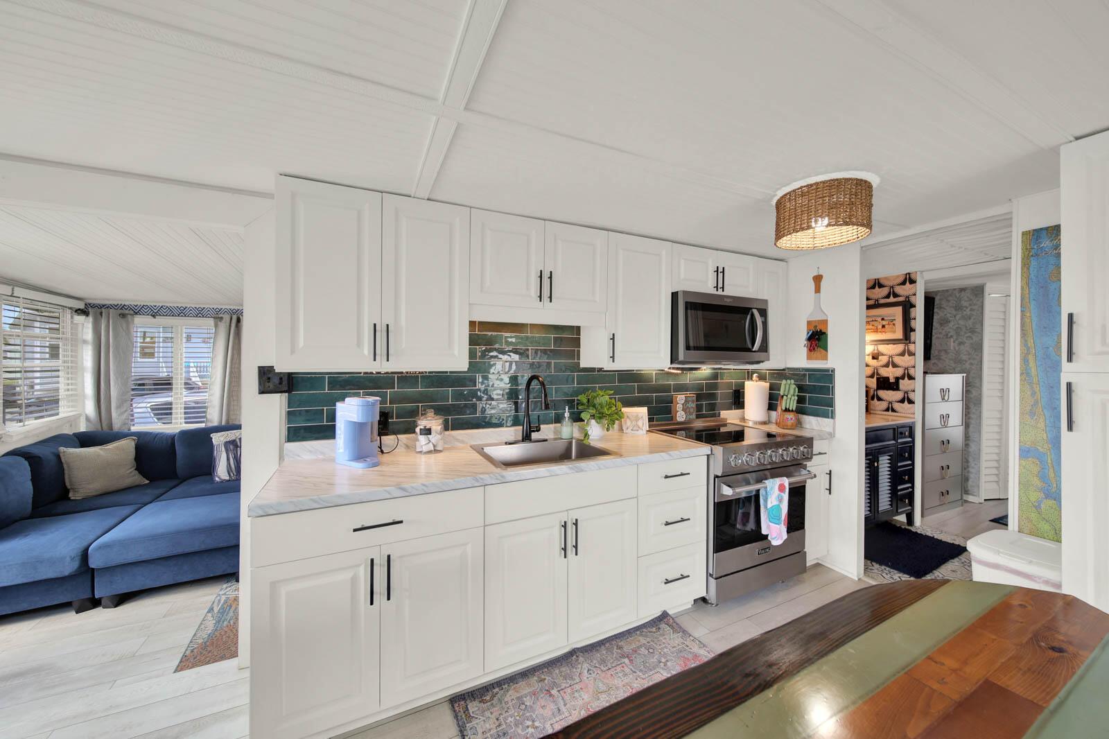 A kitchen features white cabinets, a green tiled backsplash, marble-look countertops, and stainless steel appliances — 833 Nettles Boulevard, Jensen Beach FL 34957, JENSEN BEACH, FL
