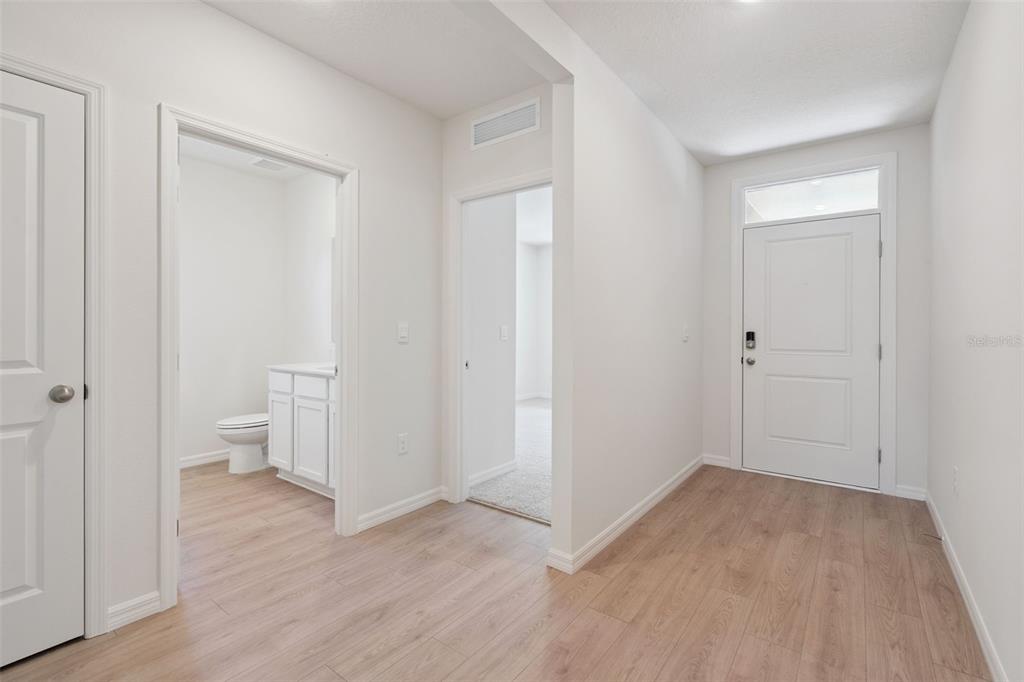 An entryway with light wood-look flooring leads to a bathroom and a carpeted room — 2516 DORSET COURT, ORMOND BEACH, FL