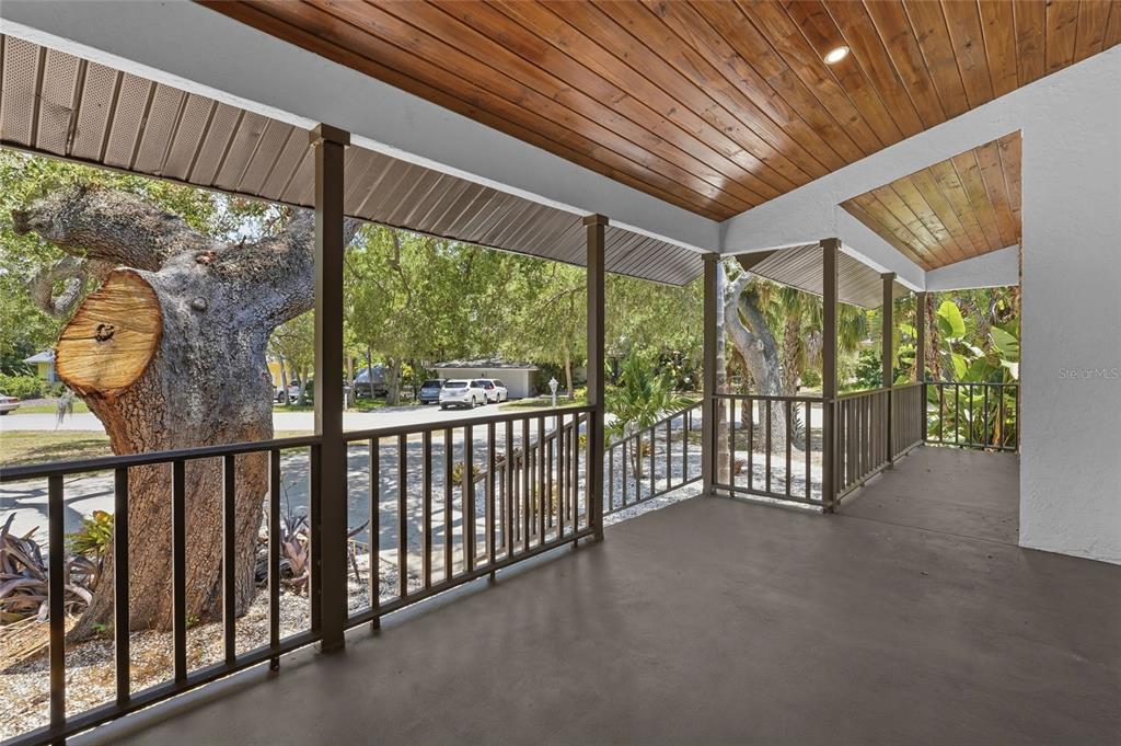 A covered porch features a wood-paneled ceiling, dark railings, and a view of trees — 4074 REDBIRD CIRCLE, SARASOTA, FL