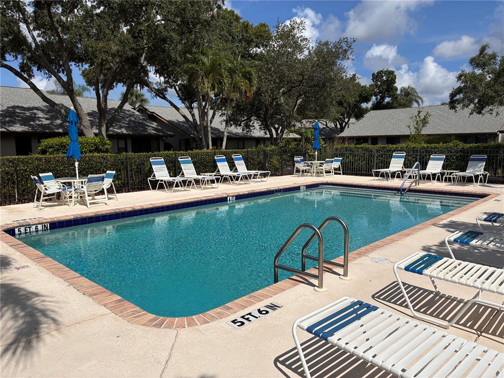 An outdoor swimming pool surrounded by lounge chairs, tables, and umbrellas on a concrete deck — 4521 KINGSMERE UNIT 6, SARASOTA, FL
