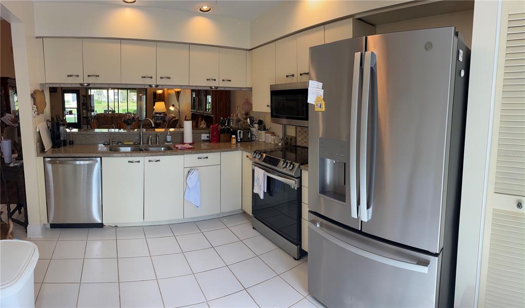 A kitchen features stainless steel appliances, light-colored cabinets, tiled flooring, and a mirrored backsplash — 4521 KINGSMERE UNIT 6, SARASOTA, FL