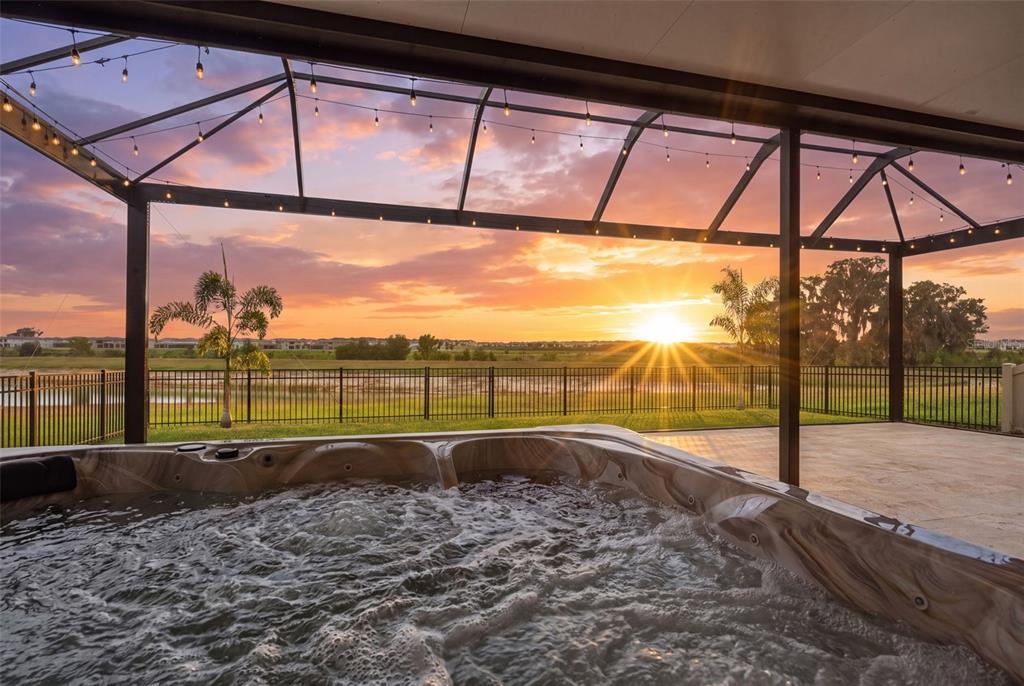 A hot tub sits on a covered patio overlooking a fenced backyard at sunset — 9663 BRANCHING SHIP TRACE, WESLEY CHAPEL, FL