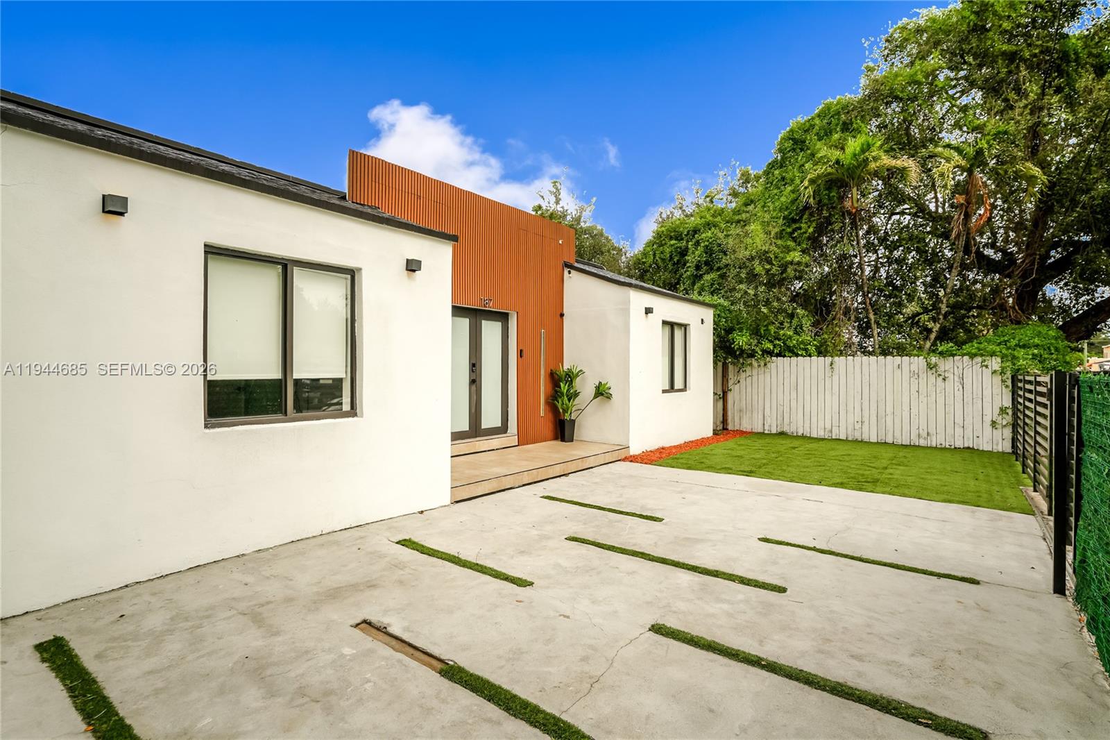 A modern white house features a wood-slat entryway and a concrete driveway with grass strips — 187 NW 53rd St, Miami FL 33127, MIAMI, FL