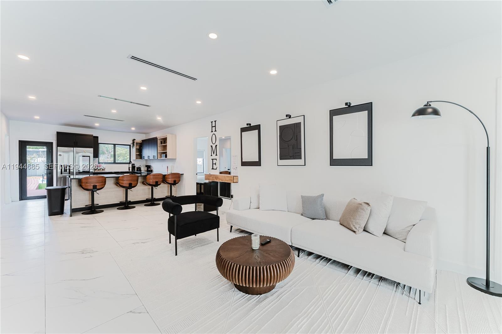 A modern open-concept living room features white tile floors, a white sofa, and a kitchen — 187 NW 53rd St, Miami FL 33127, MIAMI, FL