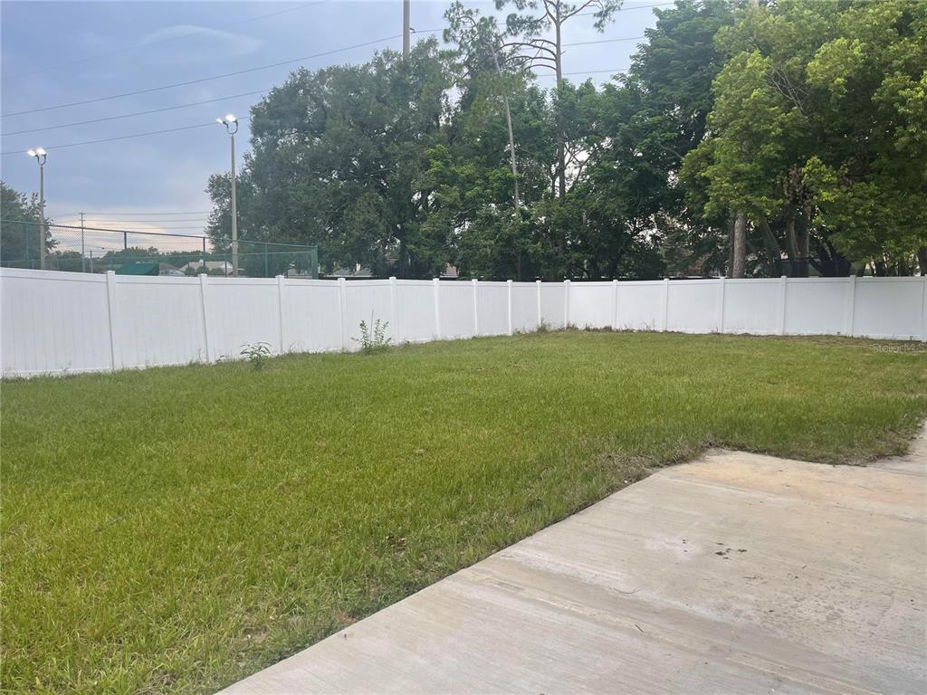 A grassy backyard features a concrete patio and is enclosed by a white vinyl fence — 9310 BAY VISTA ESTATES BOULEVARD, ORLANDO, FL