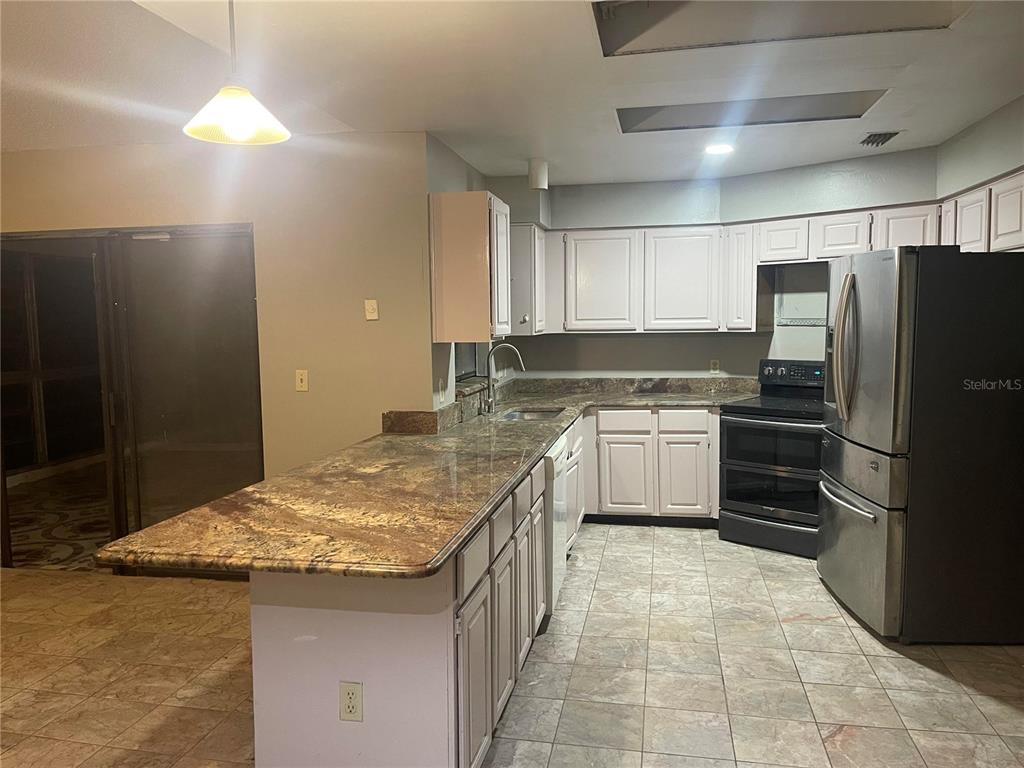 A kitchen features white cabinets, granite countertops, stainless steel appliances, and tile flooring — 9310 BAY VISTA ESTATES BOULEVARD, ORLANDO, FL