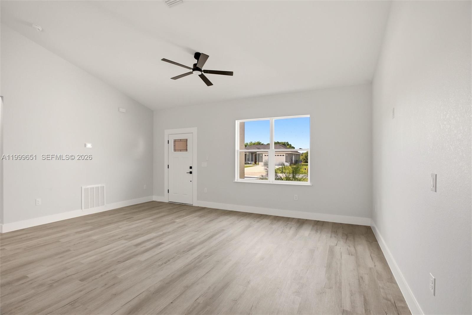 A bright, empty room features light wood-look flooring, a ceiling fan, and a front door — 1313 Blue Heron Drive, Sebring FL 33876, SEBRING, FL