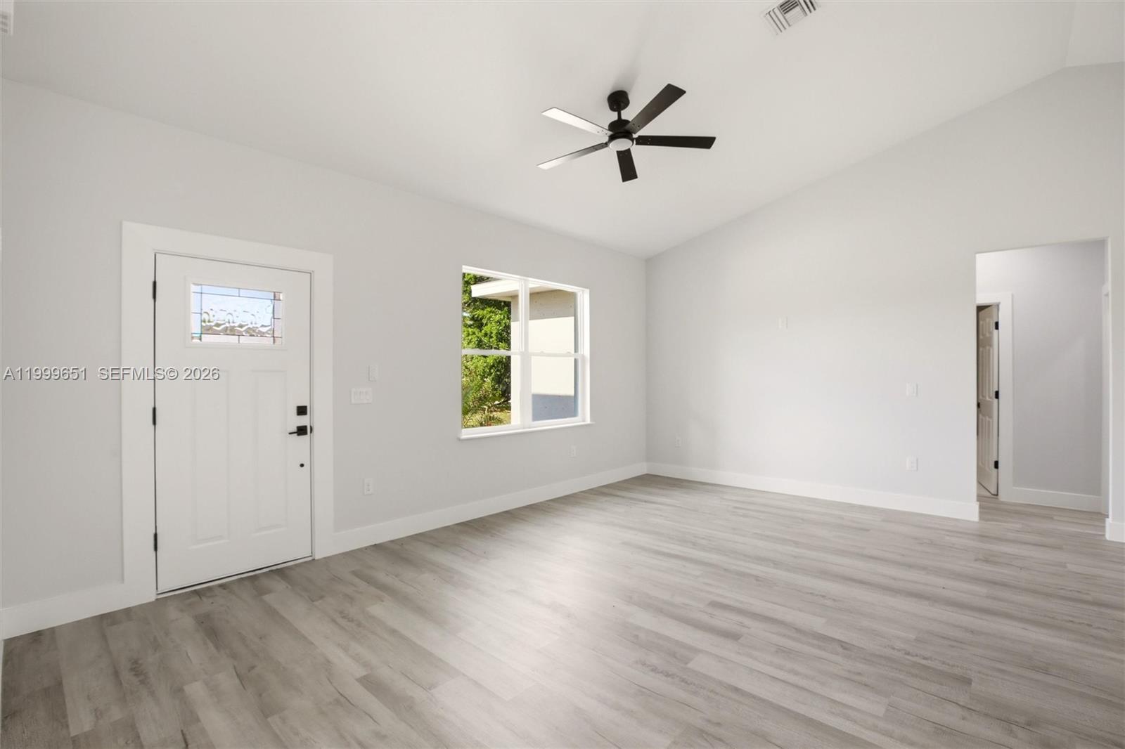 An empty room features light gray walls, wood-look flooring, a ceiling fan, and a door — 1313 Blue Heron Drive, Sebring FL 33876, SEBRING, FL