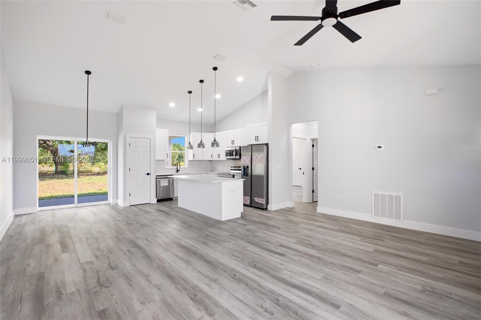 A modern open-concept kitchen and living area features white cabinetry, stainless steel appliances, and wood-look flooring — 1313 Blue Heron Drive, Sebring FL 33876, SEBRING, FL