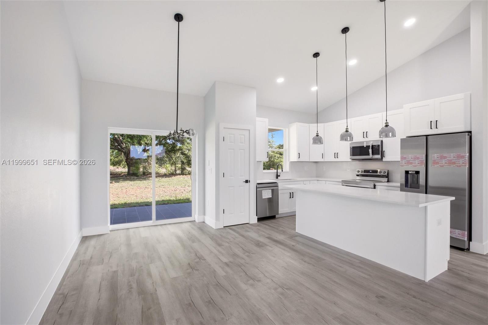 A modern kitchen with white cabinetry, stainless steel appliances, and gray wood-look flooring — 1313 Blue Heron Drive, Sebring FL 33876, SEBRING, FL