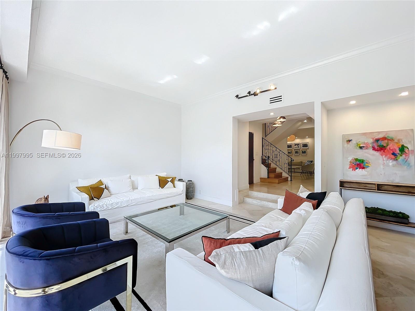 A bright living room features white sofas, blue armchairs, a glass coffee table, and stairs — 201 Crandon Blvd # 163, Key Biscayne FL 33149, KEY BISCAYNE, FL