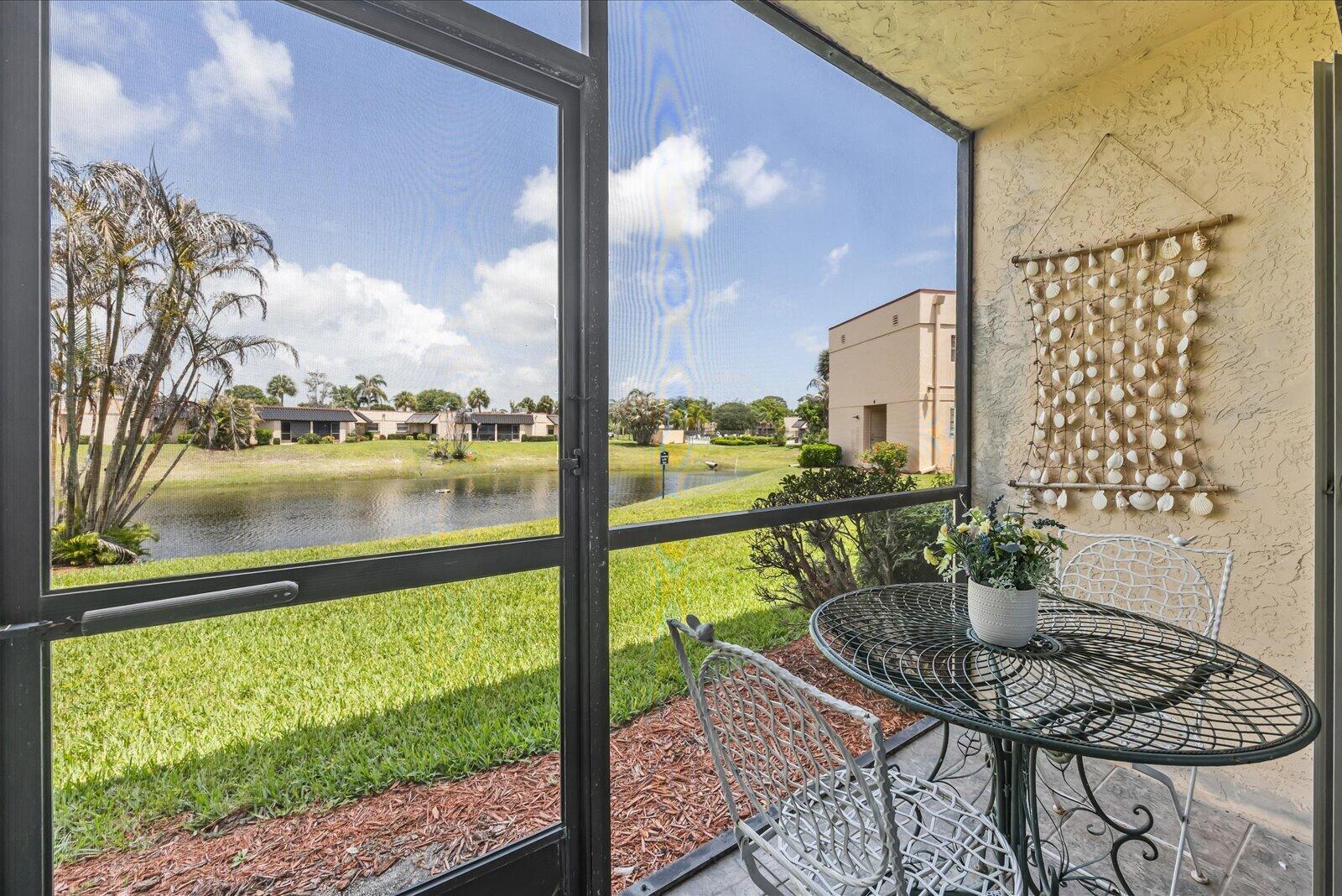 A screened-in patio features a metal bistro set overlooking a pond and residential buildings — 2069 NE Collins Circle # 50, Jensen Beach FL 34957, JENSEN BEACH, FL
