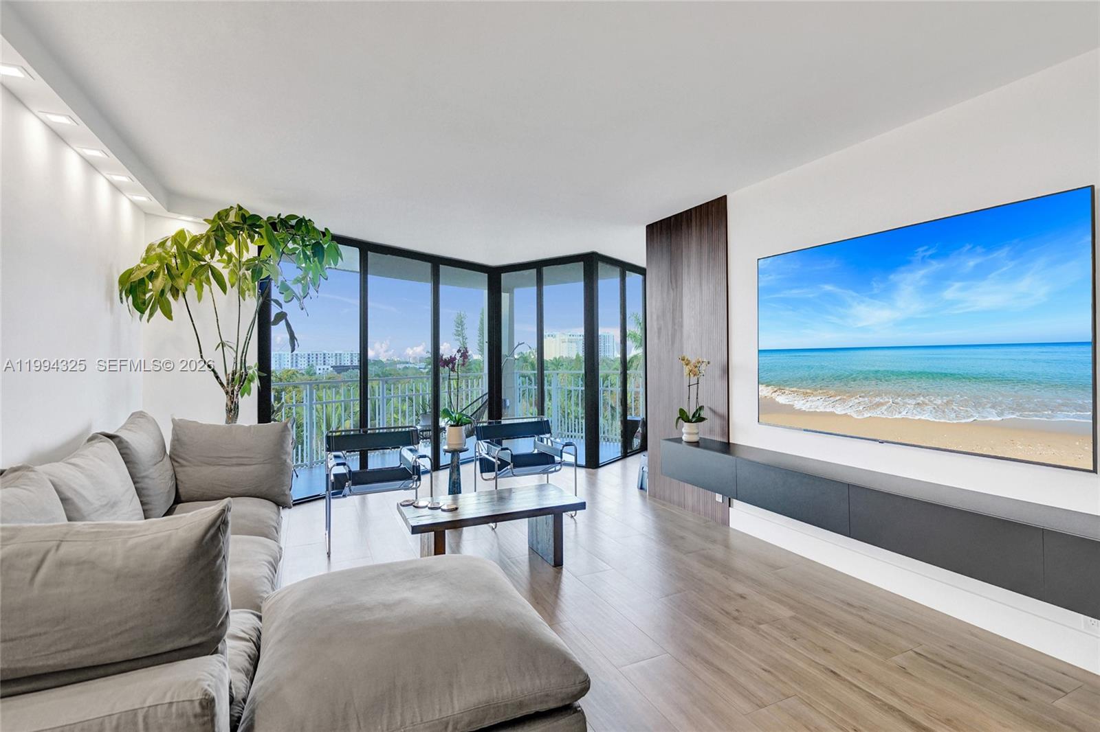 A modern living room features a large sectional sofa, wood flooring, and floor-to-ceiling windows — 1000 Quayside Ter # 707, Miami FL 33138, MIAMI, FL