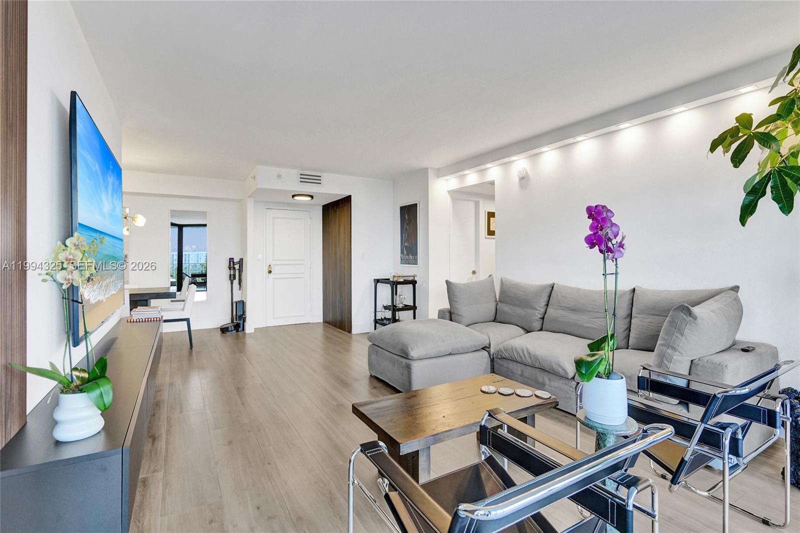 A modern living room features a grey sectional sofa, wood coffee table, and light flooring — 1000 Quayside Ter # 707, Miami FL 33138, MIAMI, FL