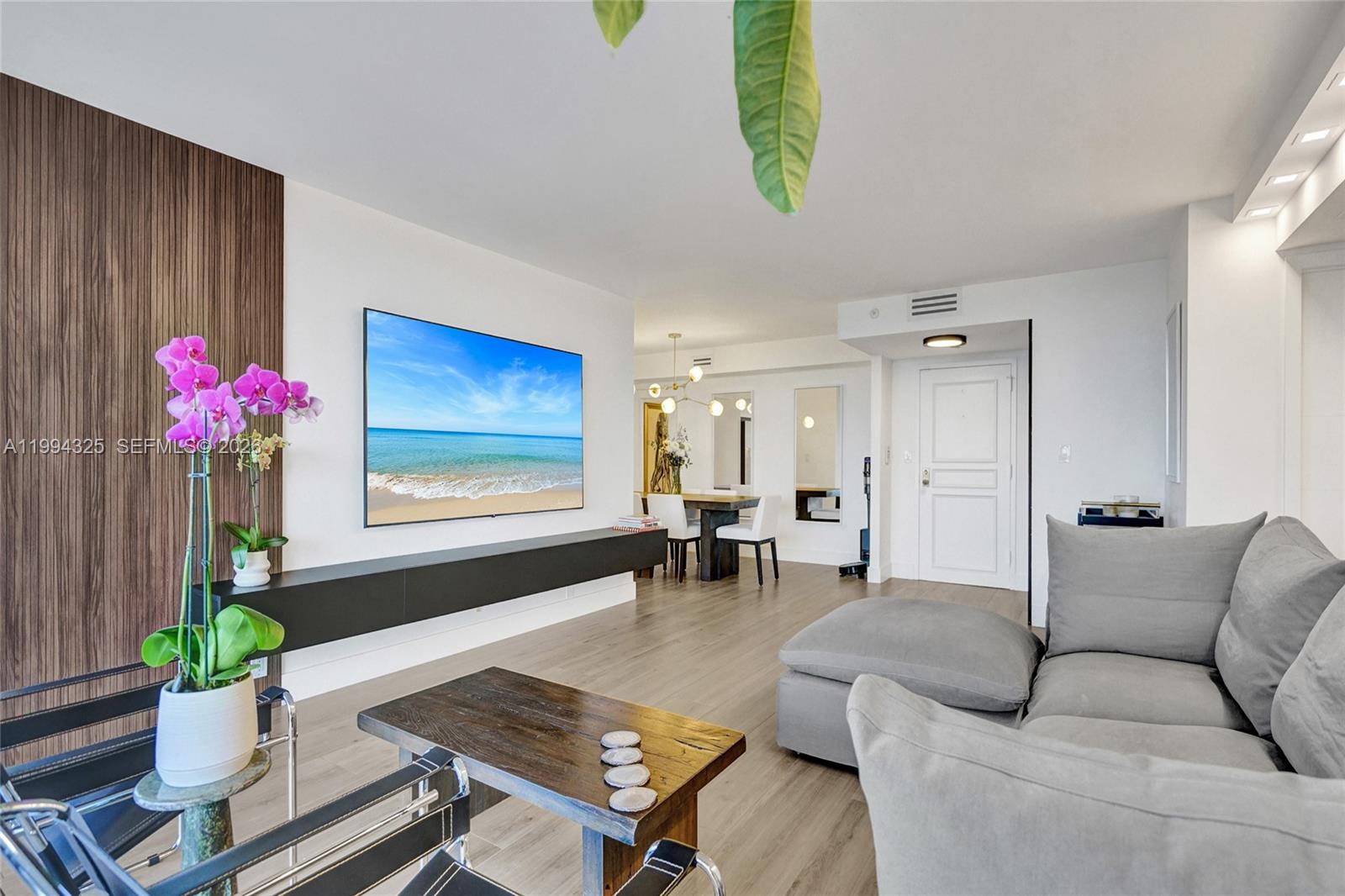 A living room features a wall-mounted television, a floating shelf, and a gray sectional sofa — 1000 Quayside Ter # 707, Miami FL 33138, MIAMI, FL